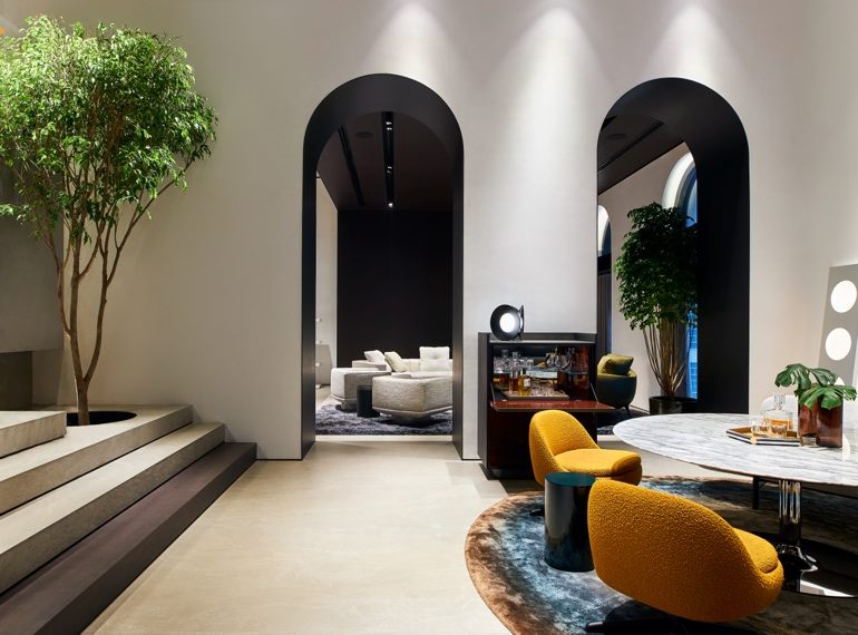 Interior of a Minotti monobrand showroom, with tall arched openings, a marble table and upholstered armchairs